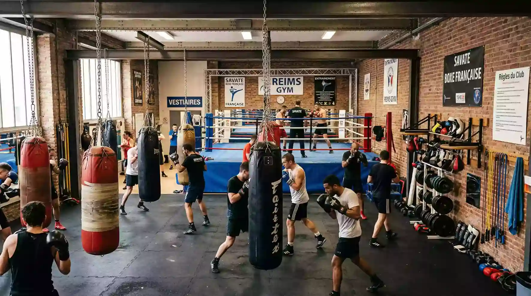 Salle d'entraînement de boxe française avec des sacs de frappe et un ring en arrière-plan